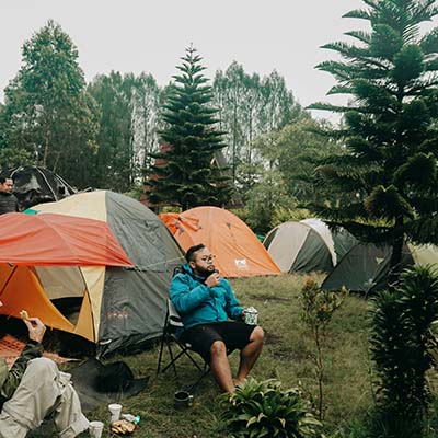Guy sitting by tents in a forest